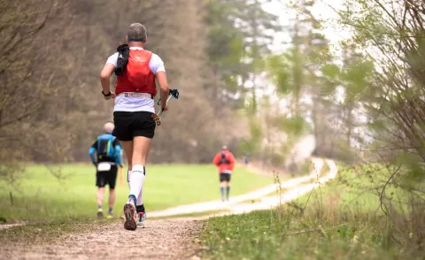 Trail runner navigating a scenic mountain path with essential gear like GLUNA trail shoes and a hydration pack.